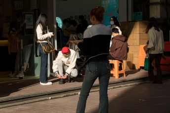 一个男子骑着滑板在街上滑行 一个女子在人行道上走过去。