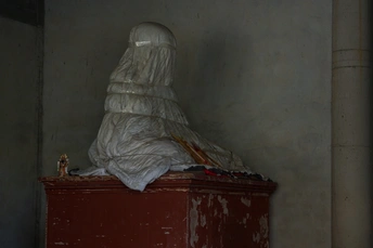 一个用塑料包装的雕像坐在红色的垃圾桶上 周围用白色塑料袋覆盖。