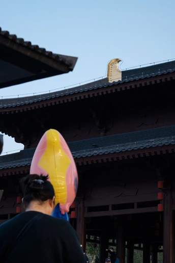 一位女子举着气球站在寺庙前 背景是有一栋建筑。