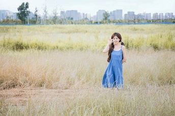 一个穿着蓝色连衣裙的年轻女子站在一片高草地上 正在用手机讲话。