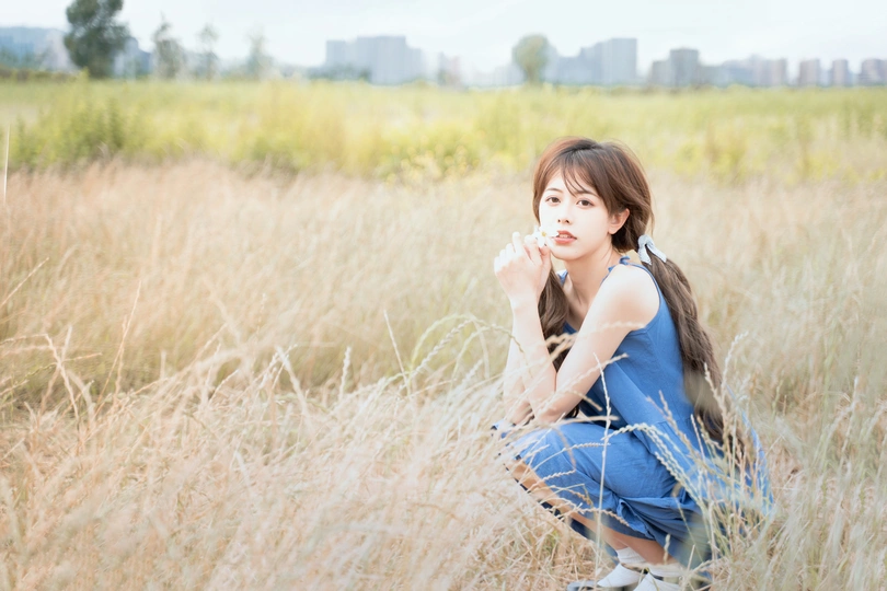 一个穿着蓝色连衣裙的年轻女子坐在一片高草地上