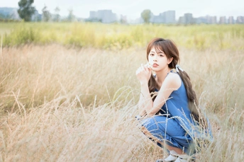 一个穿着蓝色连衣裙的年轻女子坐在一片高草地上