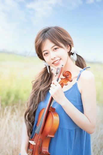蓝色连衣裙的年轻女子在田野中拉小提琴的肖像