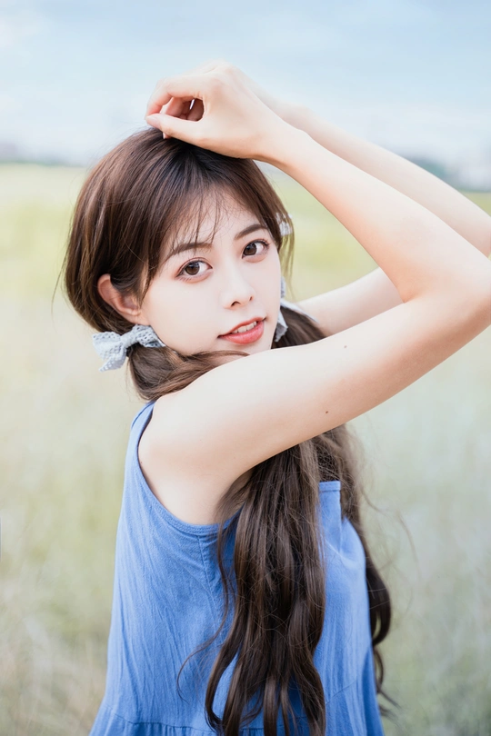 一位长发年轻女子穿着蓝色连衣裙站在田野中的人物肖像