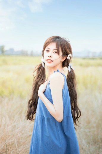 一位长发年轻女子穿着蓝色连衣裙站在田野中的人物肖像