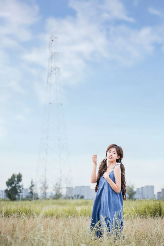 一位穿着蓝色连衣裙的年轻女子站在一片高草丛中