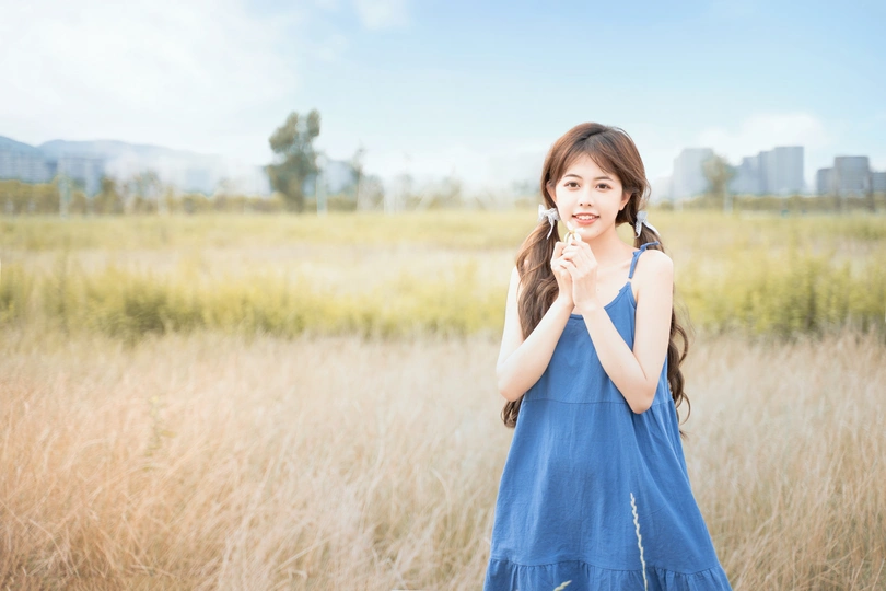 一位穿着蓝色连衣裙的年轻女子站在一片高草丛中