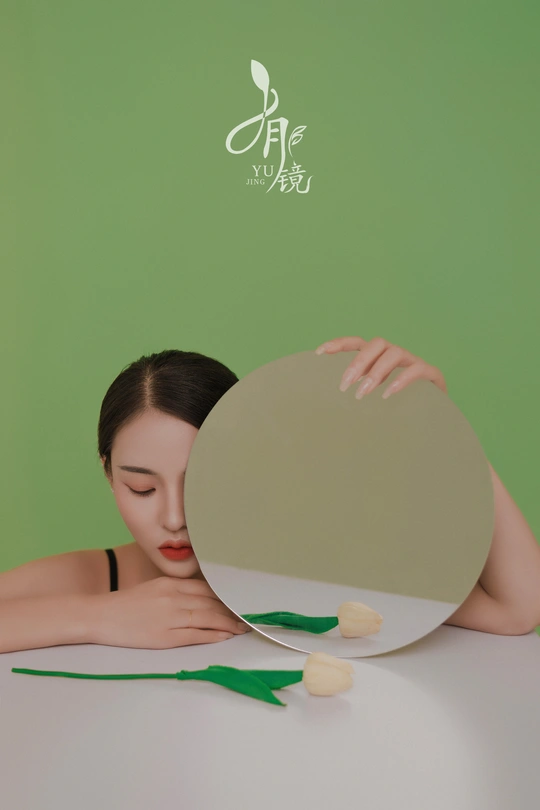 一位年轻女子拿着一朵白花看着镜子里的倒影