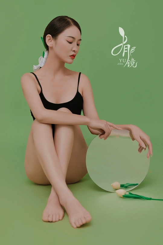 一位穿着黑色衣服的年轻女子交叉着腿站在绿色镜子前