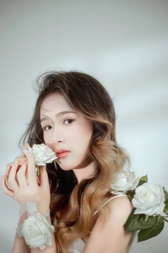 一位美丽的年轻女子穿着白色连衣裙 手里拿着一朵白色玫瑰。