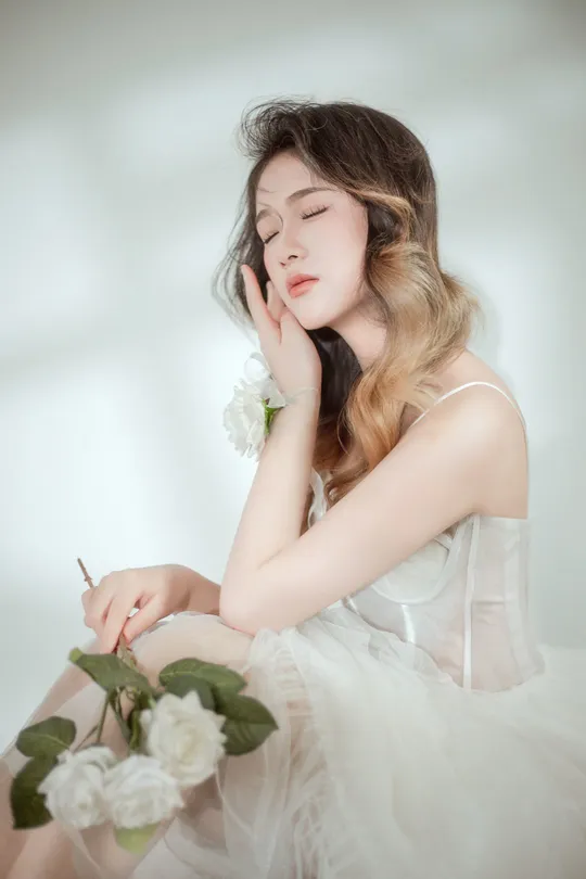 一位穿着白色连衣裙的年轻女子手里拿着一朵花