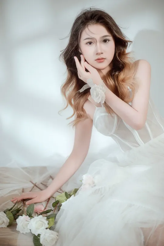 一位穿着白色连衣裙的美丽年轻女子坐在地板上 背景是新娘的肖像 白色背景照片