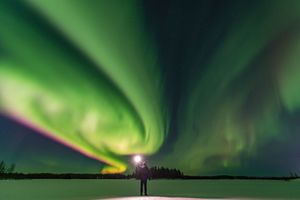 一个人站在天空中的一片绿色极光前面