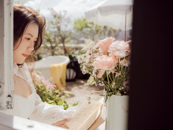 一位美丽的年轻女士正在窗台上摆放着白色花朵凝视着窗外。