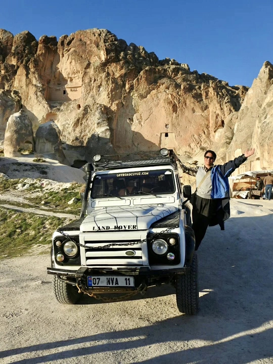 一个站在泥土路上 前面有一辆汽车和一辆卡车 背景有悬崖和岩石的男子。