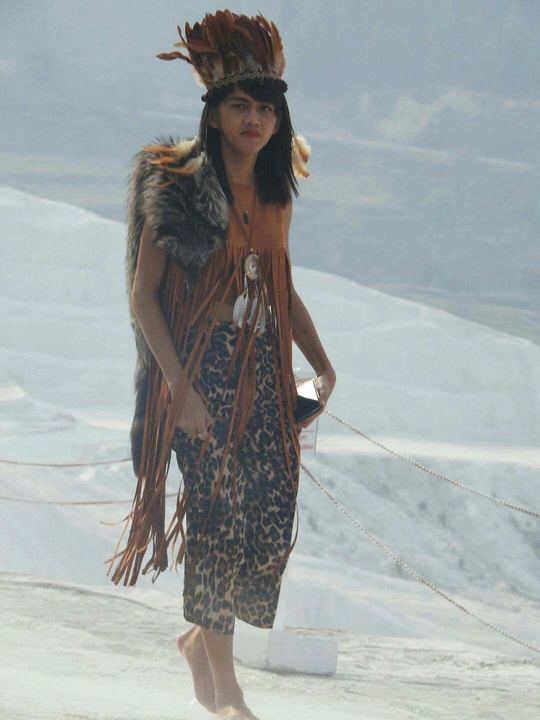 一个穿着土著服装和帽子的人在雪中站立。