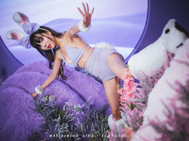 一个年轻女子躺在粉红色的床上 周围堆放着毛绒玩具 正在为拍照做姿势。