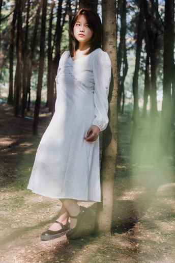 一个穿着白色连衣裙的年轻女子站在森林里