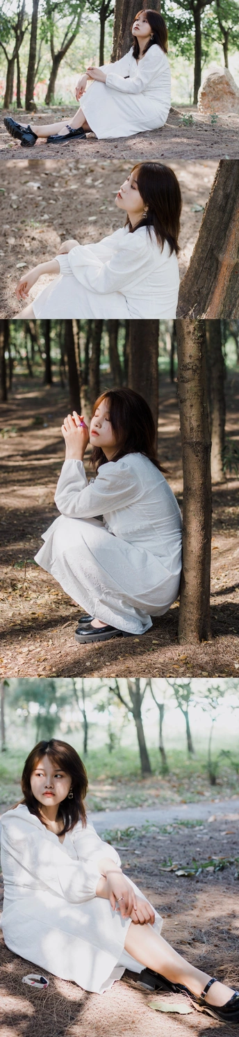 一个穿着白色连衣裙的年轻女子坐在树林里的地上