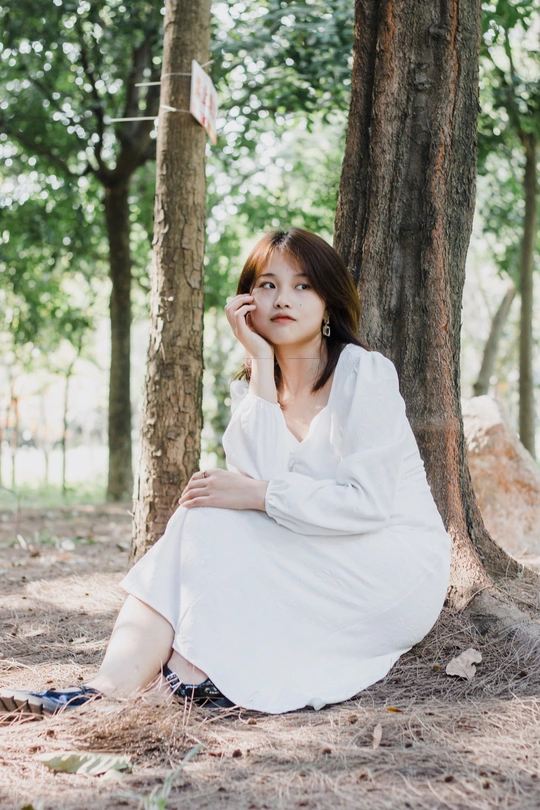 一个穿着白色连衣裙的年轻女子坐在树林里的一棵树下