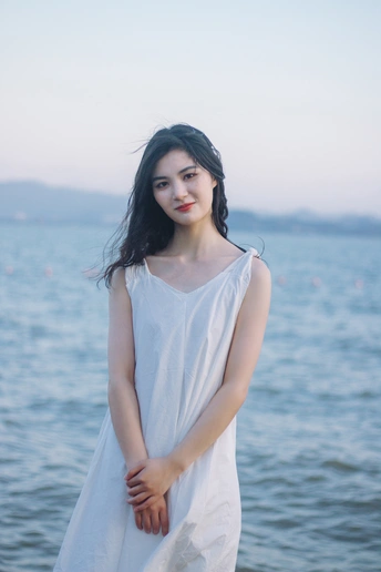 穿着白色连衣裙的年轻美女站在海滩水边的肖像