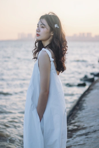 一位身穿白衬衫的年轻女子站在码头上 背景是大海