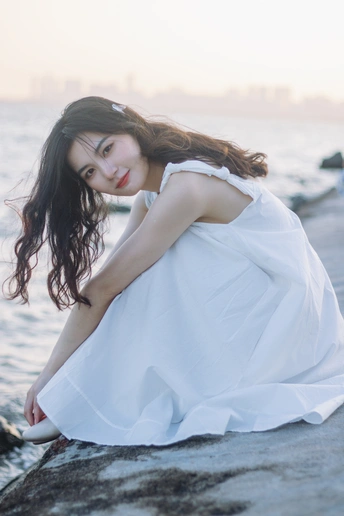 一个穿着白色连衣裙的年轻女子坐在海边或海边的岩石上