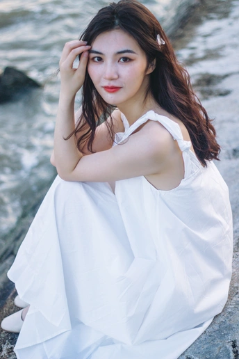 穿着白色连衣裙的美丽年轻女子坐在水边的岩石上