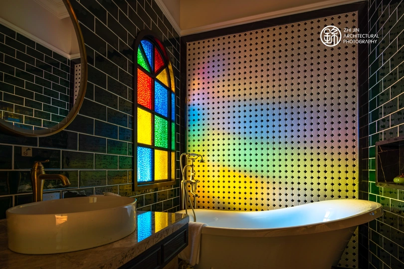 一个多彩的浴室 配有水槽、浴缸、镜子和墙上镶嵌的彩色玻璃窗。