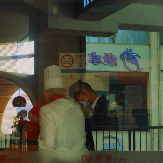 一个餐厅 一个人在柜台前做饭 透过窗户看着一对站在它前面的夫妇。