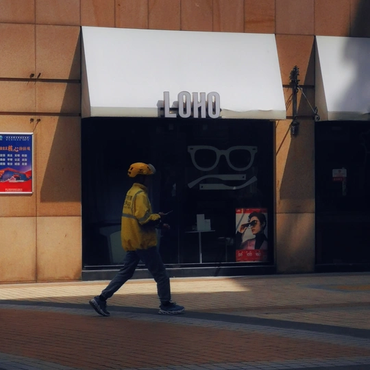 一名穿着黄色衣服的行人走在商店前的人行道上。