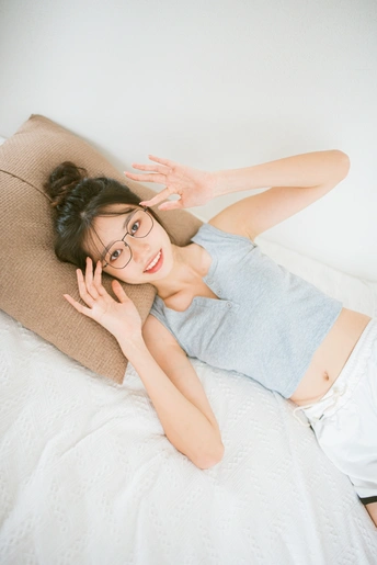 一位戴着眼镜的年轻女子躺在白色的床上对着镜头摆姿势