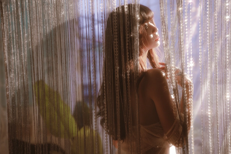 一个穿着连衣裙的年轻女子站在一个光线昏暗的房间里 面前有一扇窗帘。