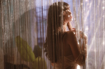 一个穿着连衣裙的年轻女子站在一个光线昏暗的房间里 面前有一扇窗帘。