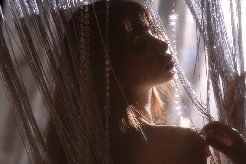 一个年轻女子在窗前挂着薄纱窗帘 背景中有灯光。