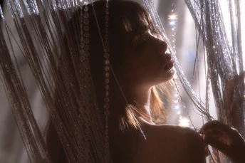 一个年轻女子在窗前挂着薄纱窗帘 背景中有灯光。