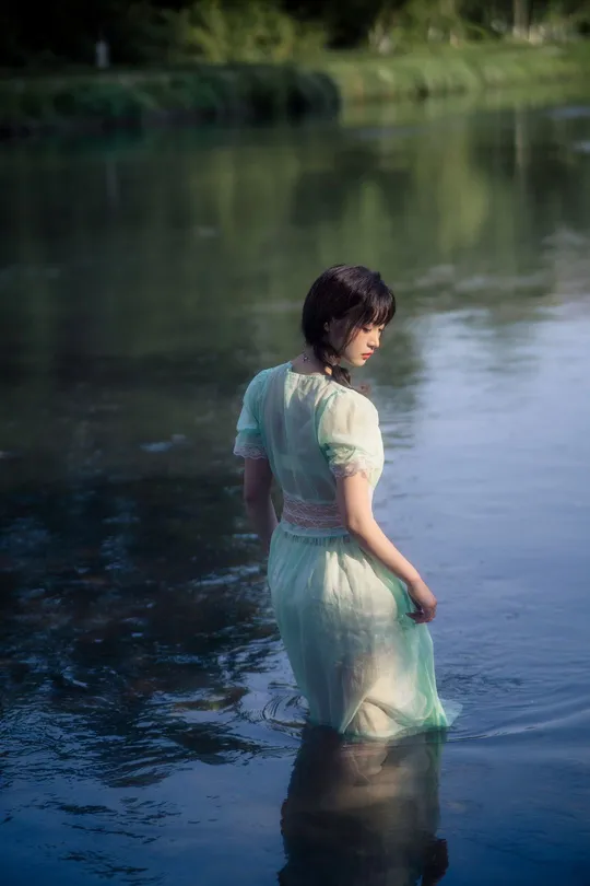 一位穿着蓝色连衣裙的年轻女子穿过湖泊的水。