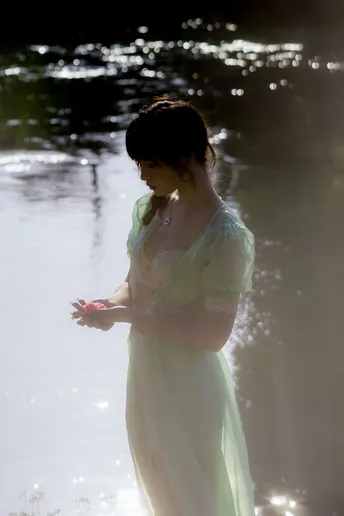 一位穿着白色连衣裙的年轻女子站在一条河流的水中 双手伸开。