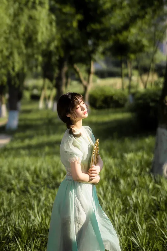 一个小女孩穿着绿色裙子手里拿着一朵花站在公园里