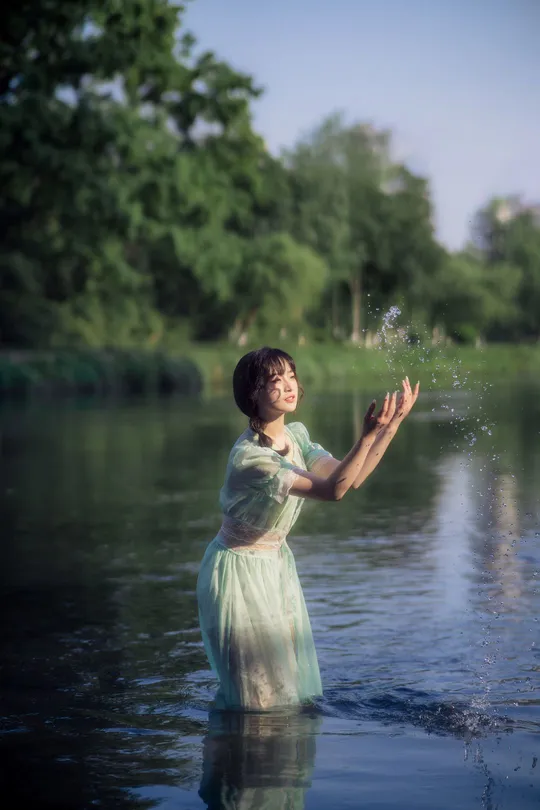 一位穿着绿色连衣裙的年轻女子站在湖中的水边。