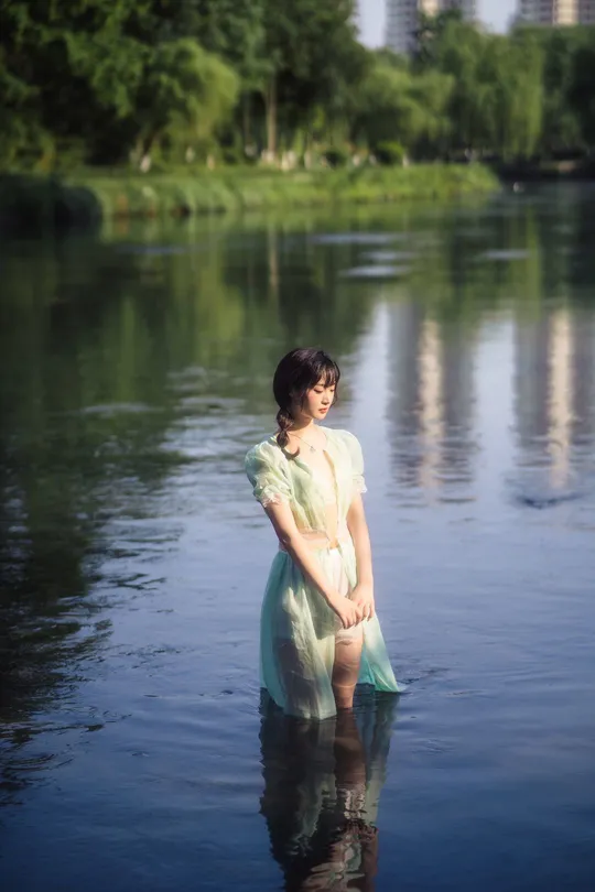 一位穿着连衣裙的年轻女子站在湖中的水边