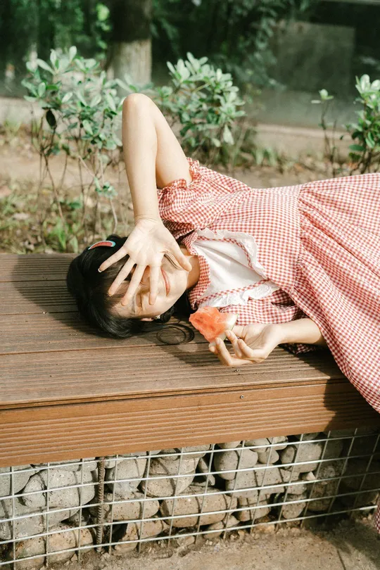 一个穿着连衣裙的年轻女子手握一只鸟儿躺在木凳上