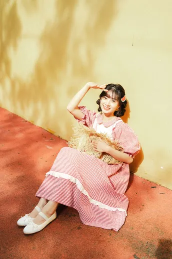 一位穿着粉红色连衣裙的年轻女子在红色墙壁前摆姿势