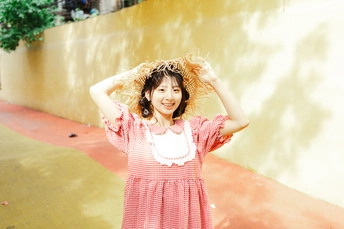 一个穿着粉红色连衣裙的小女孩站在黄色墙壁前 头戴草编帽子。