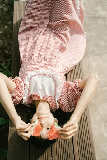 一个穿粉红色裙子的女孩坐在木凳上 手里拿着一块西瓜。