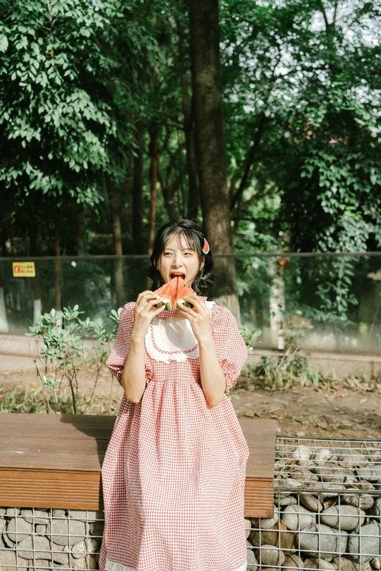 一位穿着粉红色裙子的年轻女子在公园里吃三明治。