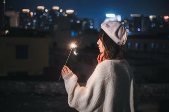 一位站在屋顶上俯瞰城市的夜晚 手持点燃的焰火的女性。