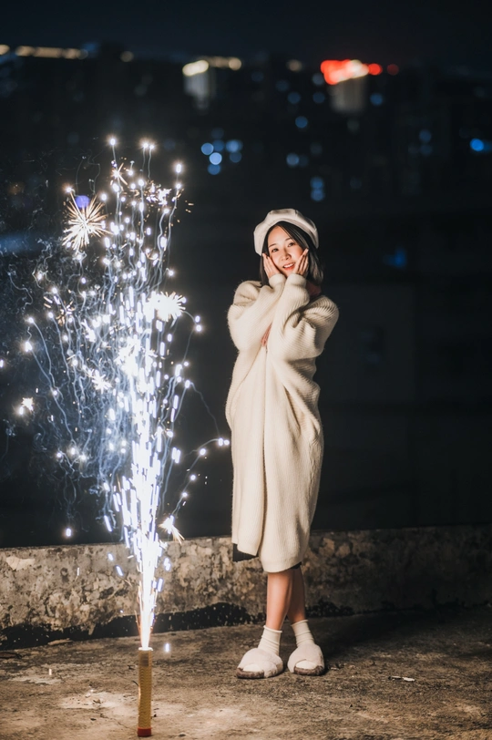站在屋顶上的夜晚 手持点燃的烟花的女青年