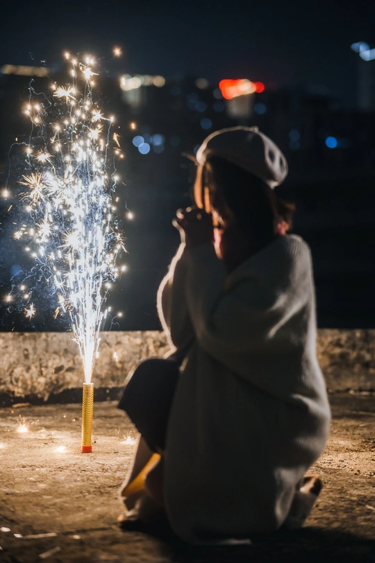 一位年轻女孩在晚上观看烟花 而另一个人拿着点燃的火花。