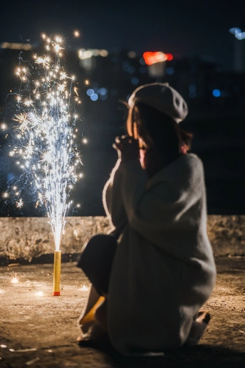 一位年轻女孩在晚上观看烟花 而另一个人拿着点燃的火花。